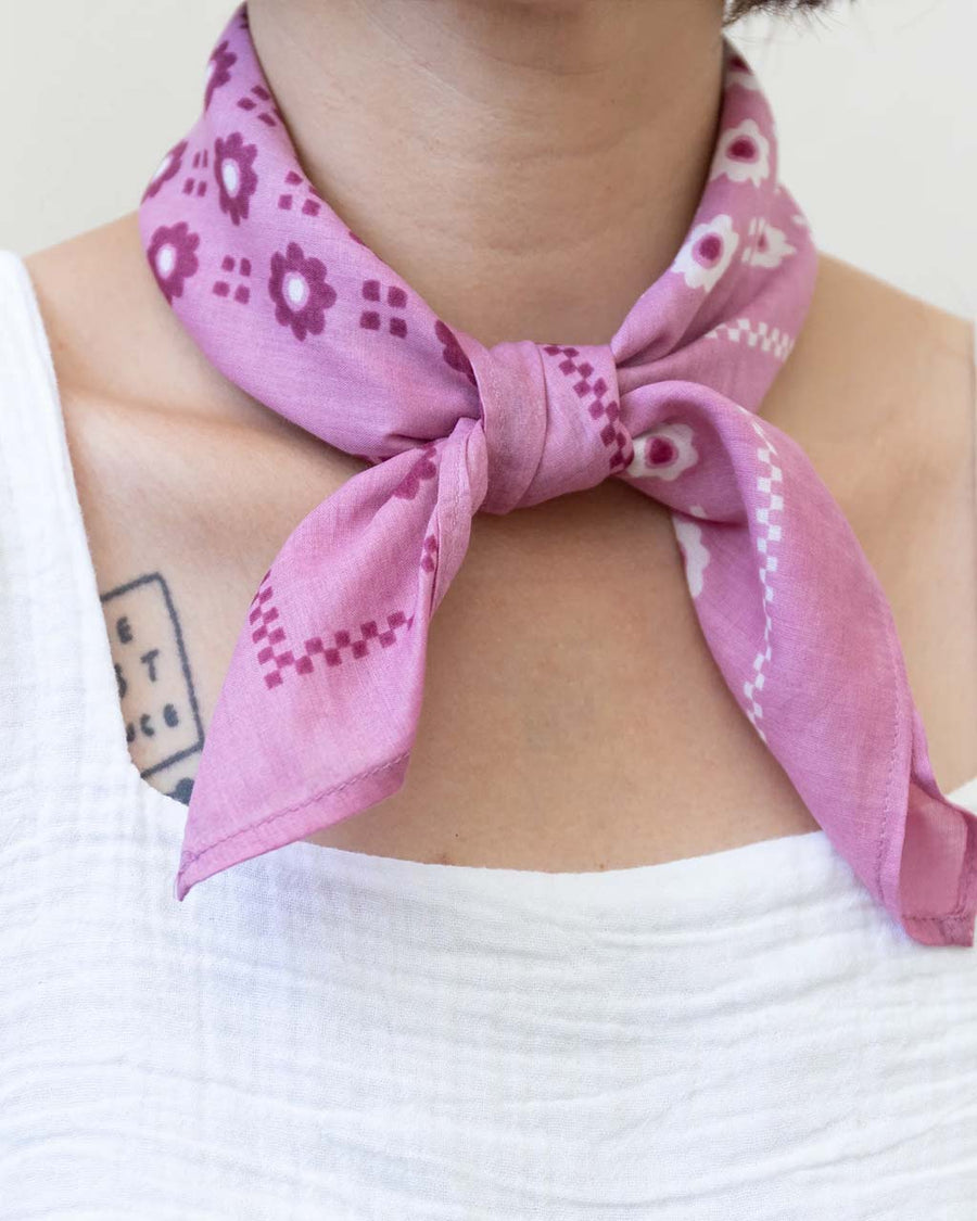 model wearing bright pink 22 in. x 22 in. square bandana with split white and plum floral print with knot on the front