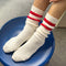 side view of model wearing white crew socks with two red stripes on the top