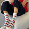 model wearing white socks with red and blue multiple stripe socks with embroidered red heart on a chair