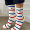 model on tip toes wearing white socks with red and blue multiple stripe socks with embroidered red heart