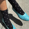side view of model wearing tall black socks with dainty white hearts and blue shoes