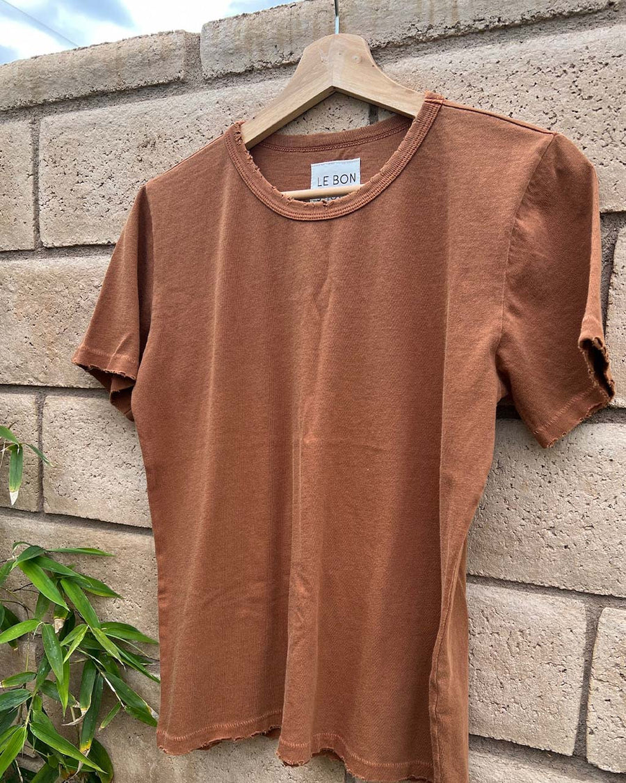 copper cotton vintage boy tee with slight distressing on the neckline and sleeves hanging on a stone wall
