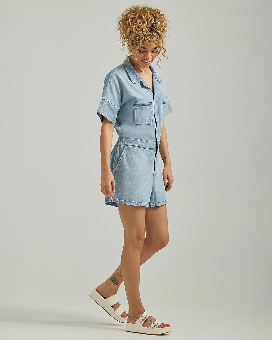 sideview of model wearing light blue denim unionall with button front, patch front pockets, and collar