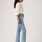 sideview of model wearing medium denim slightly relaxed straight leg jeans with cream blouse