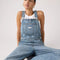 up close of model wearing light denim relaxed fit overalls with front pockets