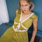 up close of model wearing chartreuse midi dress with white lace accents on the bust, two tie front and ruffle detail on the shoulders