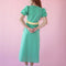 back view of model wearing green puff sleeve v-neck midi dress with pale yellow ruffle under the bust