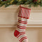 cream and red striped stocking with striped cuff and red pom detail hanging from a mantle