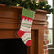 tan cotton stocking with green cuff, ed trim, and mixed print stripes in red and green hanging from a mantle