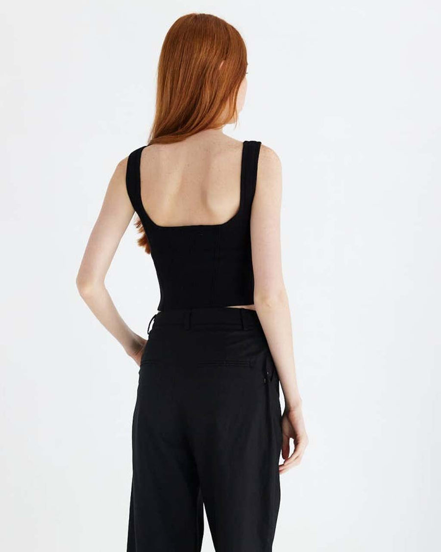 back view of model wearing black structured sleeveless crop top with piping detail