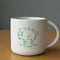 white ceramic mug with green buffalo that says 'much like the mighty buffalo, i have no f***ing money on a table