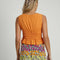 back view of model wearing orange peplum top with lace detail on the waist and side ties