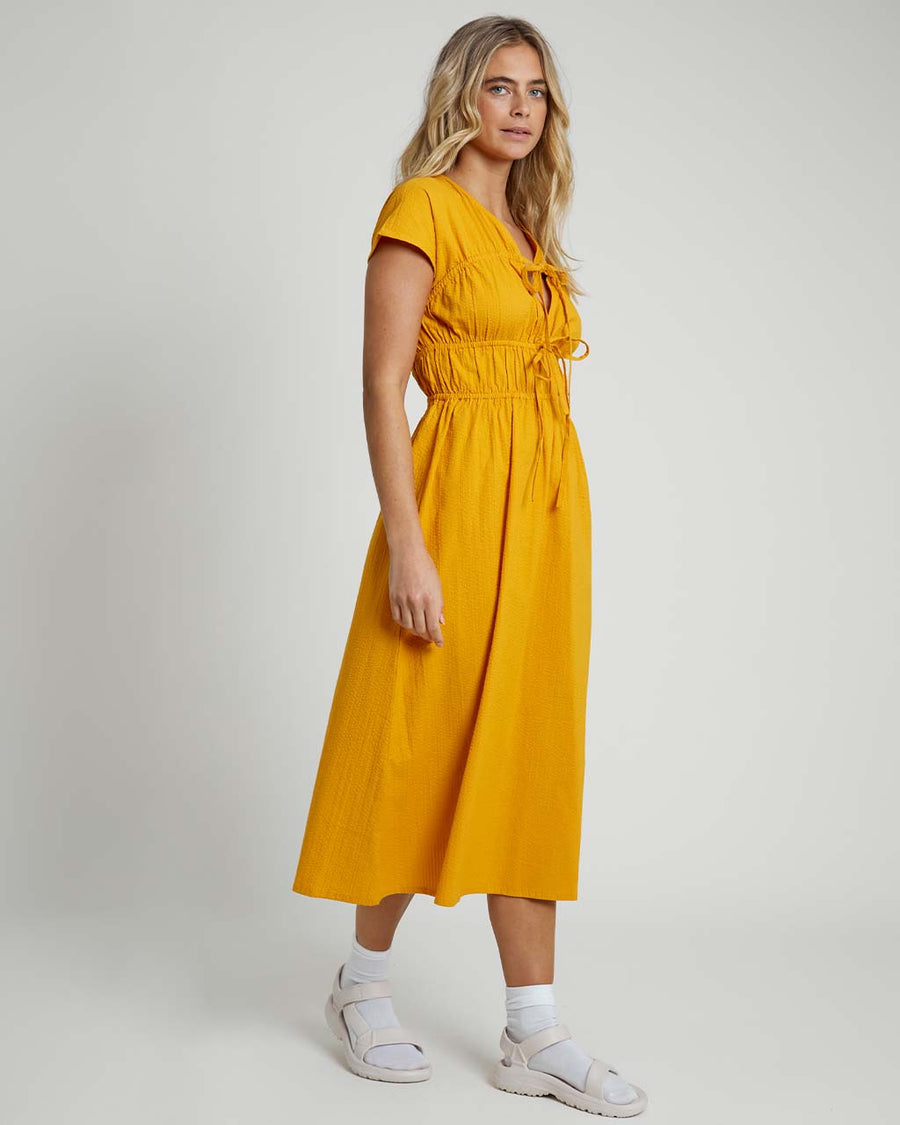 side view of model wearing yellow seer sucker midi dress with short sleeves and two tie bodice front