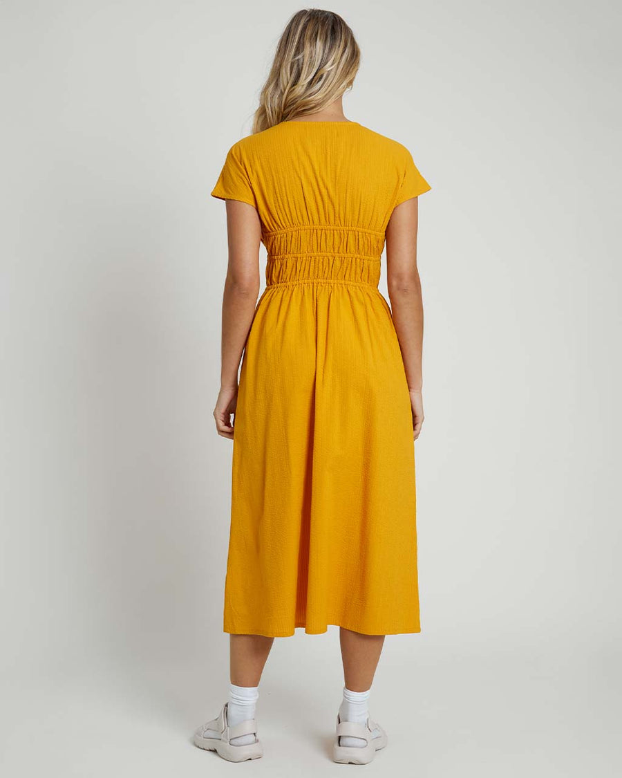 back view of model wearing yellow seer sucker midi dress with short sleeves and two tie bodice front