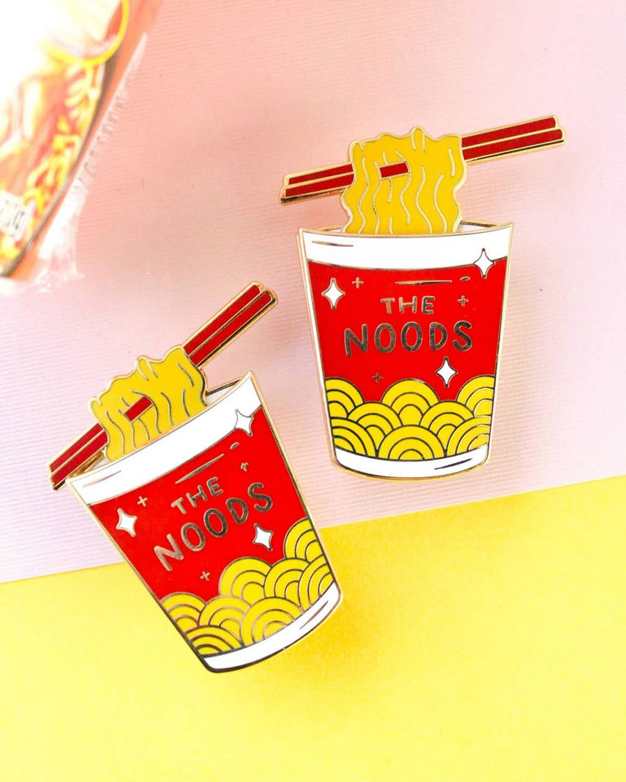 interactive enamel pin with red 'the noods' container and moveable noodle piece