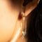 up close of model wearing gold safety pin earrings with heart detail