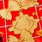 set of 4 pasta linen napkins: 2 raviolis and 2 bow tie pasta on a red tiled table