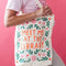 model holding tan canvas bag with orange 'meet me at the library' surrounded by colorful flowers
