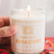 model holding soy candle with pale yellow and white vertical stripe label and says 'smells like a bookstore' across the front
