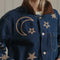 up close of model wearing denim oversized jacket with corduroy collar, patch pockets, and embroidered star, moon and sun pattern