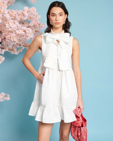 model wearing white mini dress with exaggerated bow neckline and ruffle hem 