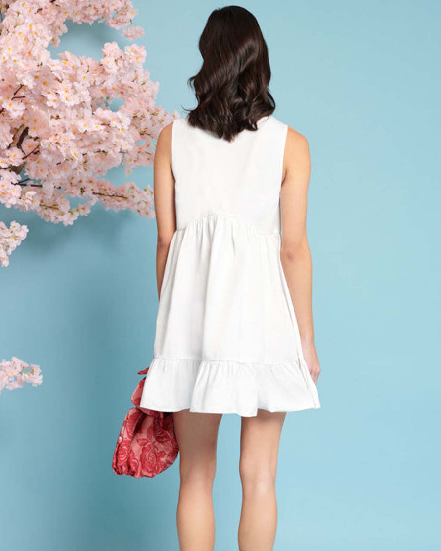 back view of model wearing white mini dress with exaggerated bow neckline and ruffle hem