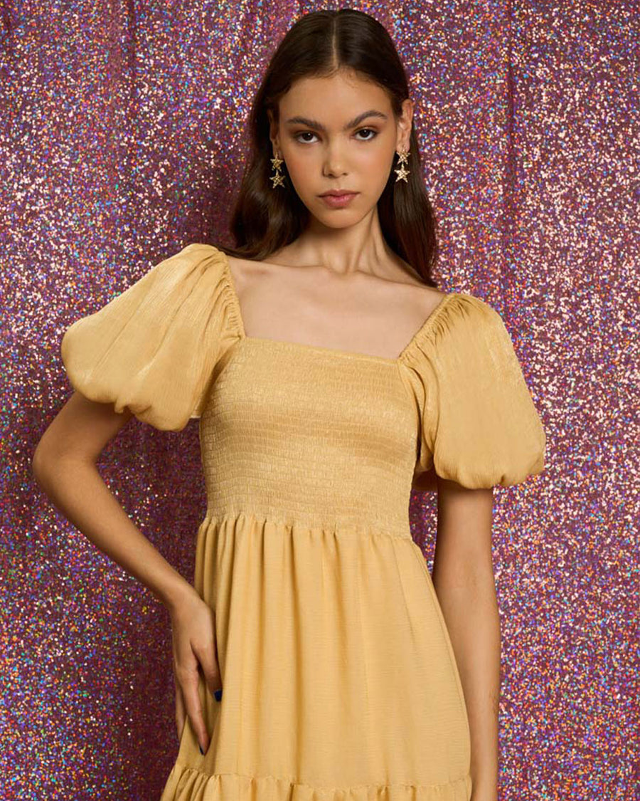 up close of model wearing golden yellow tiered midi dress with puff sleeves, smocked bodice, and back oversized bow