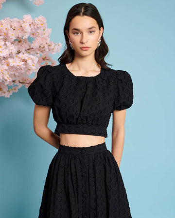 model wearing black jacquard crop top with slight puff short sleeves and tie back