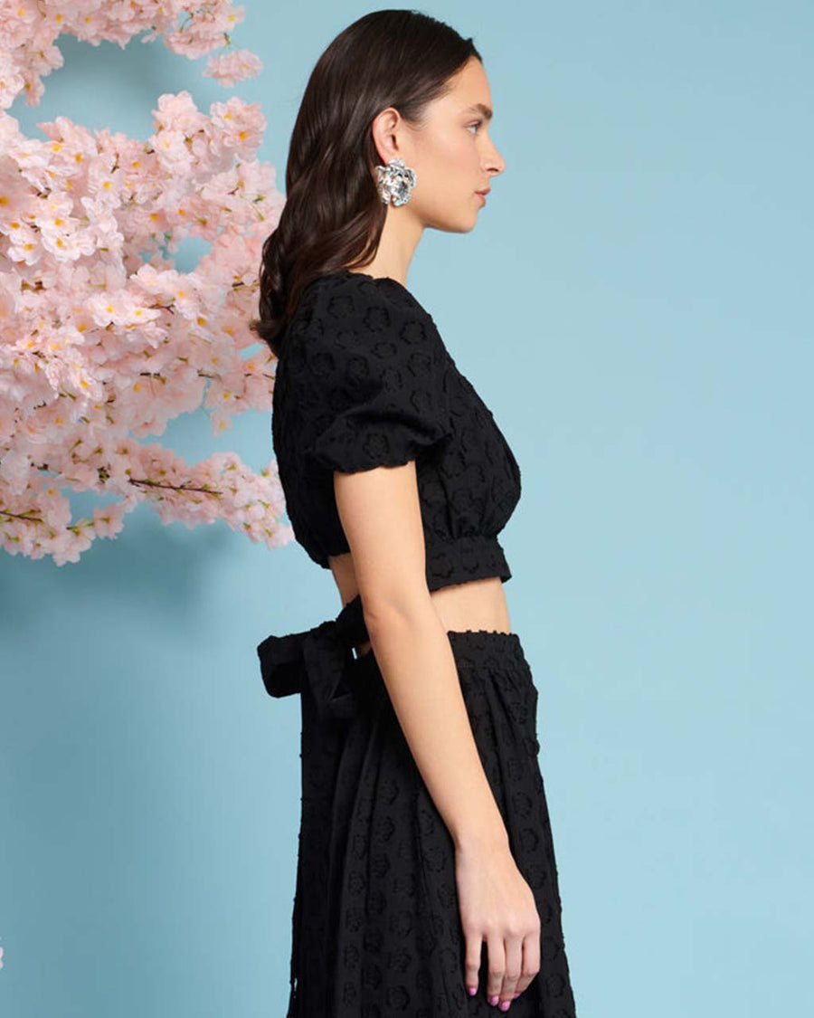 side view of model wearing black jacquard crop top with slight puff short sleeves and tie back