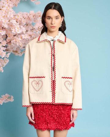 model wearing natural jacket with red ric rac trim and embroidered heart detail on front patch pockets
