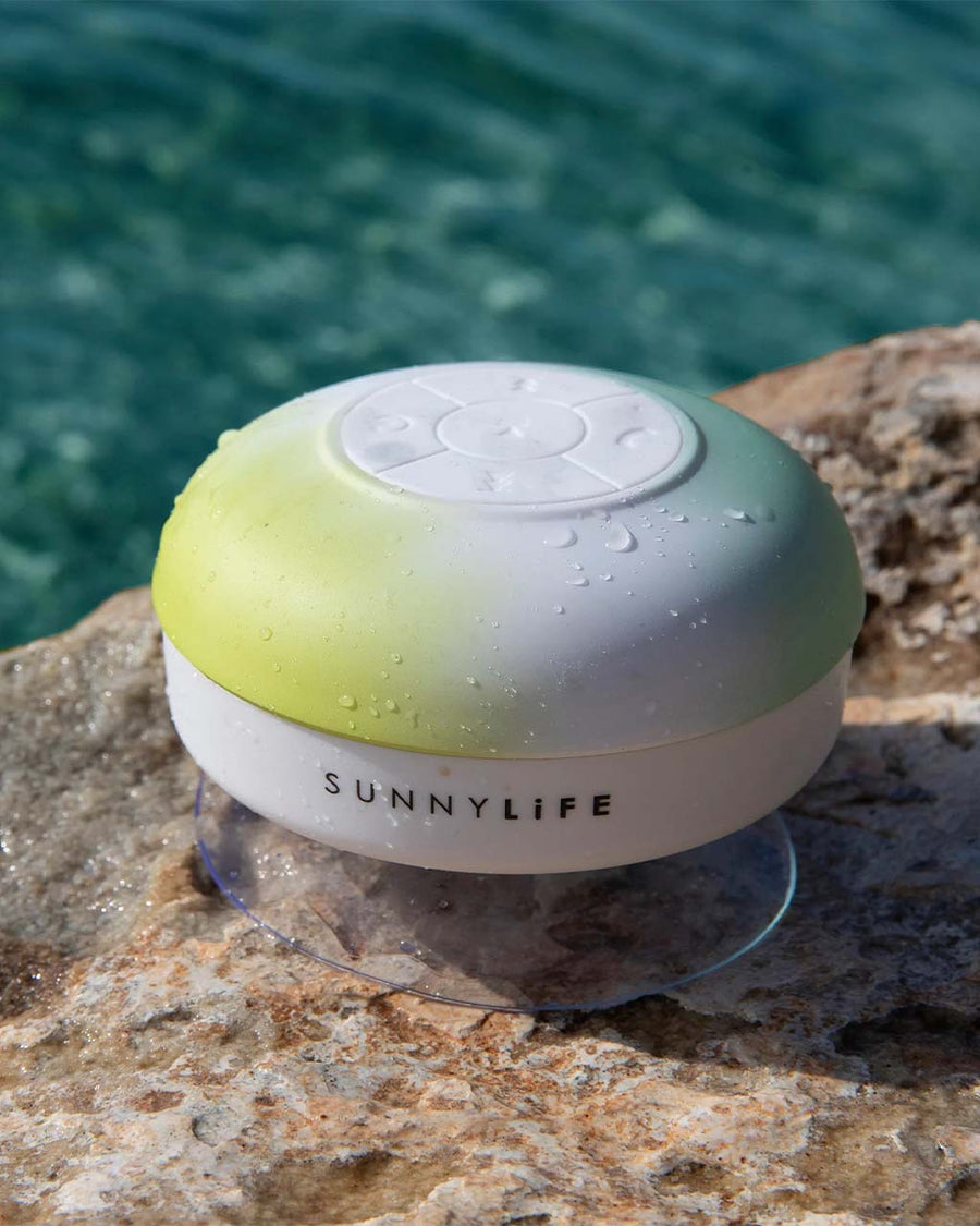 yellow, white and green circular waterproof speaker on a rock