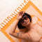 model laying on orange and white retro flower towel with tassels on the end