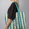 model carrying blue, white and yellow plaid large recycled plastic tote bag with ric rac detail and embroidered three fishies on the front pocket