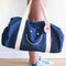model holding denim duffle bag with white smiley face and white straps