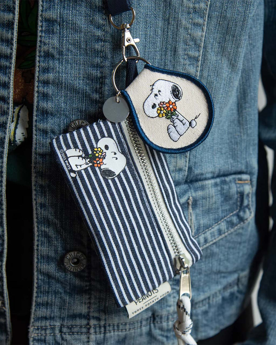 model wearing blue and white striped zip lanyard wallet with snoopy holding a bouquet of flowers