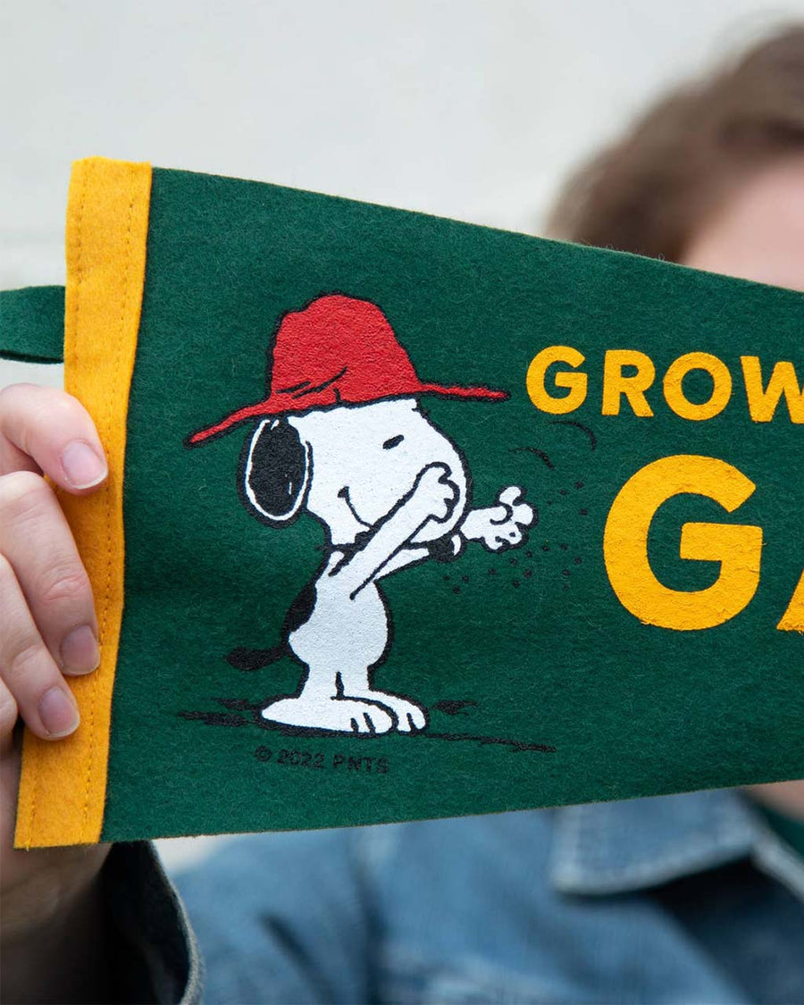 green pennant flag with snoopy graphic and gold trim and 'grow a garden' typography