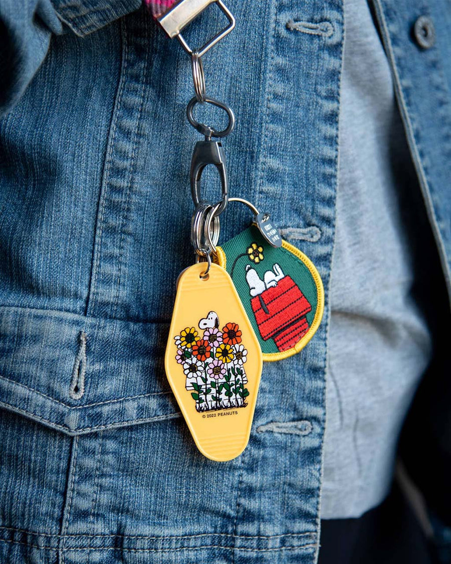 model wearing dark green patch keychain with snoopy on his doghouse looking up at a flower