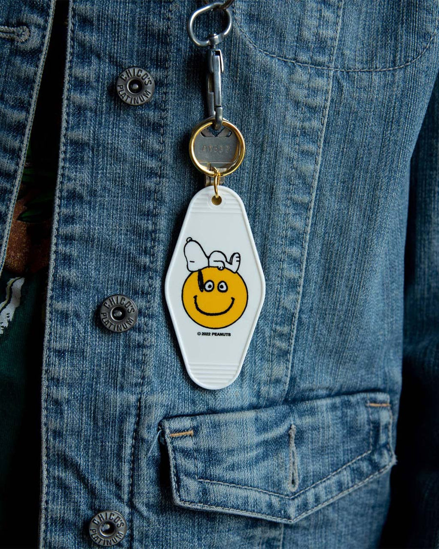 model wearing white key tag with snoopy laying on a yellow smiley face graphic