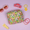 green quilted makeup bag with colorful abstract floral print surrounded by face cream, sunglasses and hair accessories