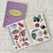 front cover and interior pages of purple and blue vertical stripe sticker book with yellow sunburst in the middle that says 'ask me about my sticker collection!'