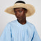 model wearing straw woven wide brim hat with open top for hair.