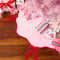 light pink tree skirt with red velvet bows and red scalloped trim with presents underneath a pink tree
