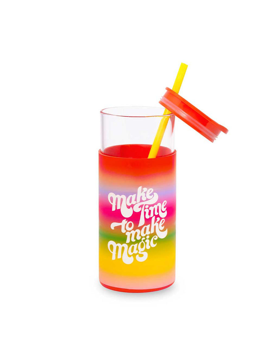 glass 20 oz tumbler with opened red lid, yellow straw, and rainbow ombre sleeve with white text 'make time to make magic' across the front