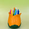 orange tulip shaped pencil holder with various pens inside