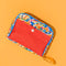 toiletry bag with red pocket and colorful fairground print on an orange background