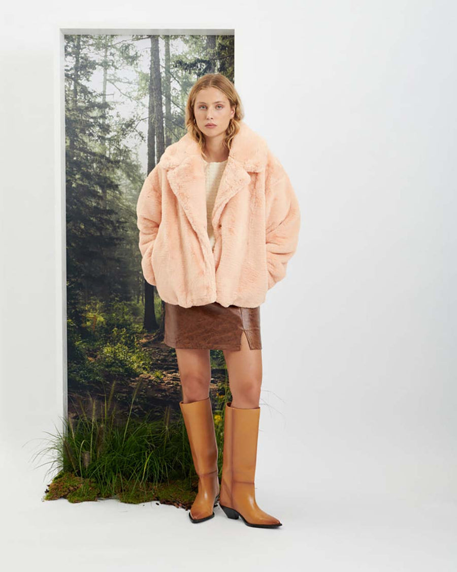 Model wearing the veronica faux fur coat standing against a forest background
