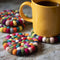 set of 4 colorful pom coasters with a coffee cup on them