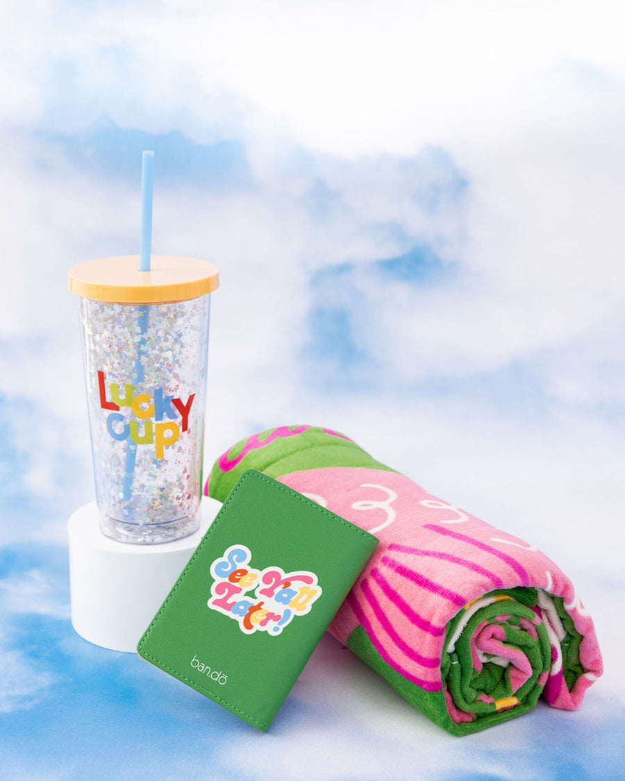 folded giant beach towel with green and white ground and vibrant sardine can print, passport holder and 'lucky cup' tumbler