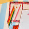 multicolor wooden pencils sitting on a notepad against a blue and white striped desktop