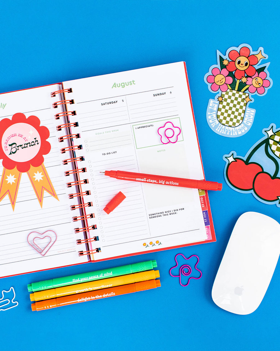 editorial image of set of 6 jumbo stickers: 'i'd rather be at brunch' ribbon,'salty' with a pretzel, 'let your happiness grow' with smiling flowers in a vase, 'tale a break' with a red heart, checkered cherry, and pink/multi disco ball, planner, markers and paper clips